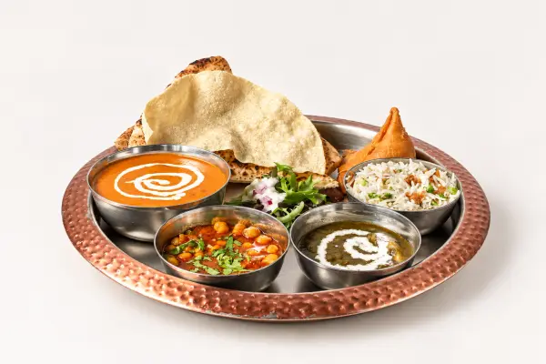 A butter chicken thali with rice, naan, poppadom and a samosa